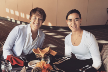 Sarah and Karin seated at a table in a room decorated with warm colors, dining.