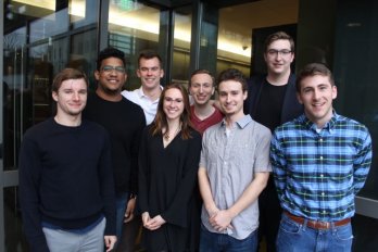 Photograph of Eight U-Mass undergraduates at 5 college geology symposium, standing in front of dimly lit hallway.