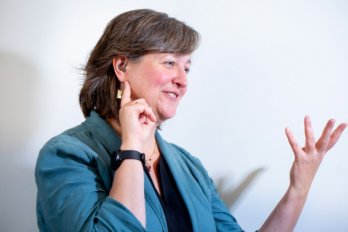 3/4 view portrait of Professor Michele Cooke gesturing to right of view, while gesturing with other hand towards her ear and hearing aid