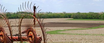 A rusty piece of farm equipment rests forlornly by barren fields.